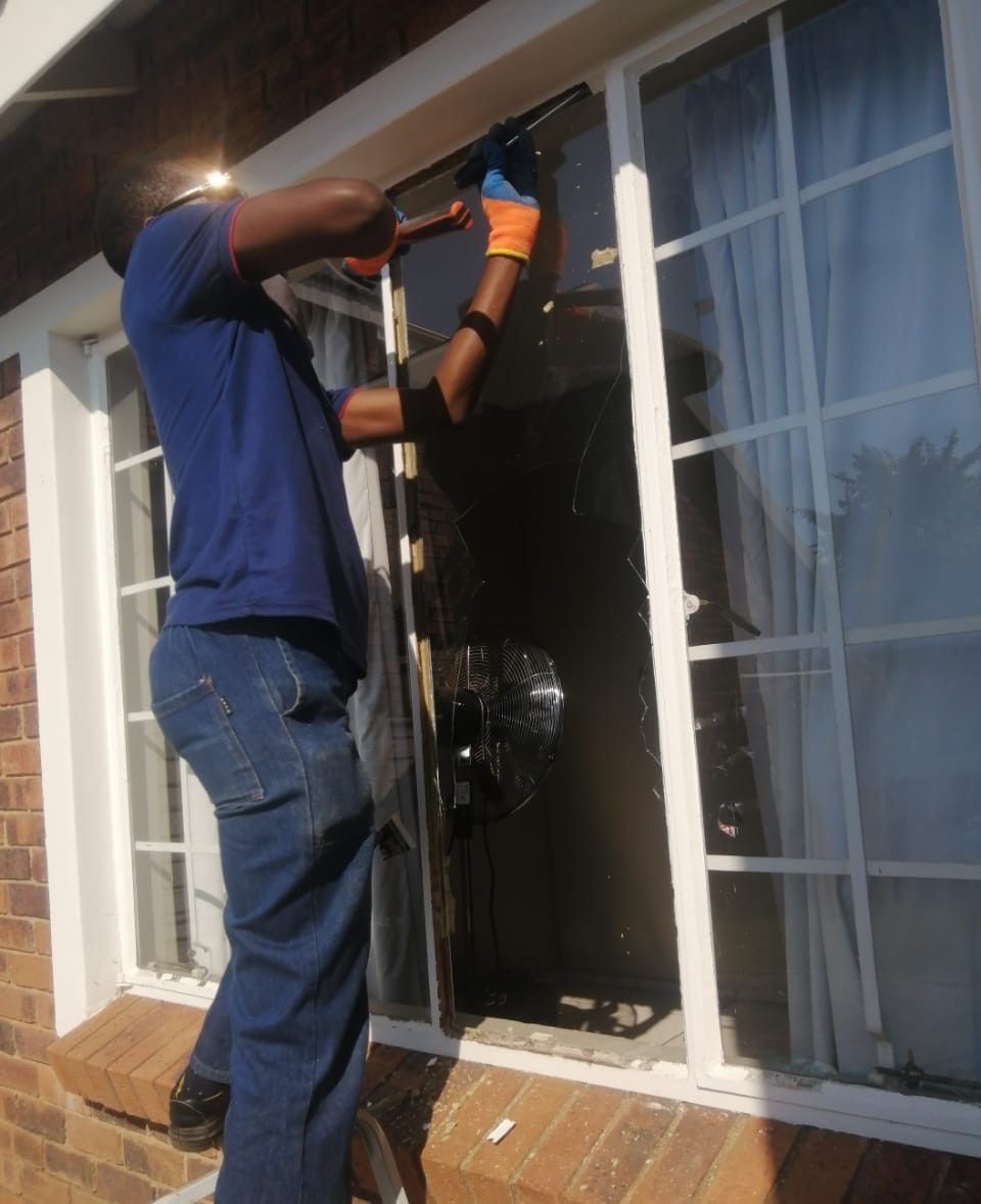 Technician taking a broken pane out of a white-framed window with glazing bars