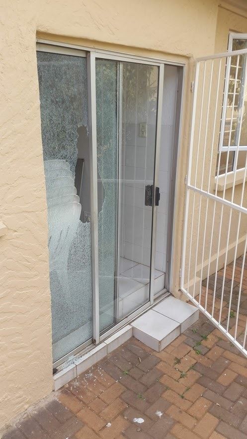Aluminium sliding door with a shattered pane beside an open security gate